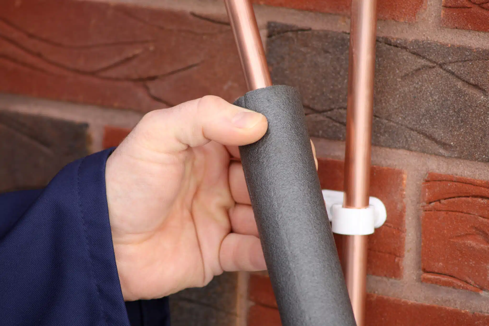 A plumber performing pipe insulation on a copper water pipe.