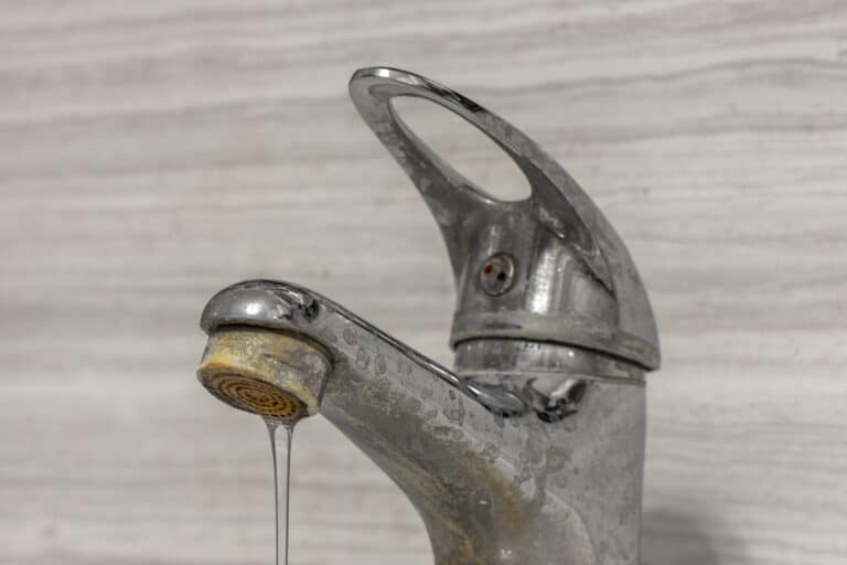 A thin stream of hard water flows from an old tap aerator.
