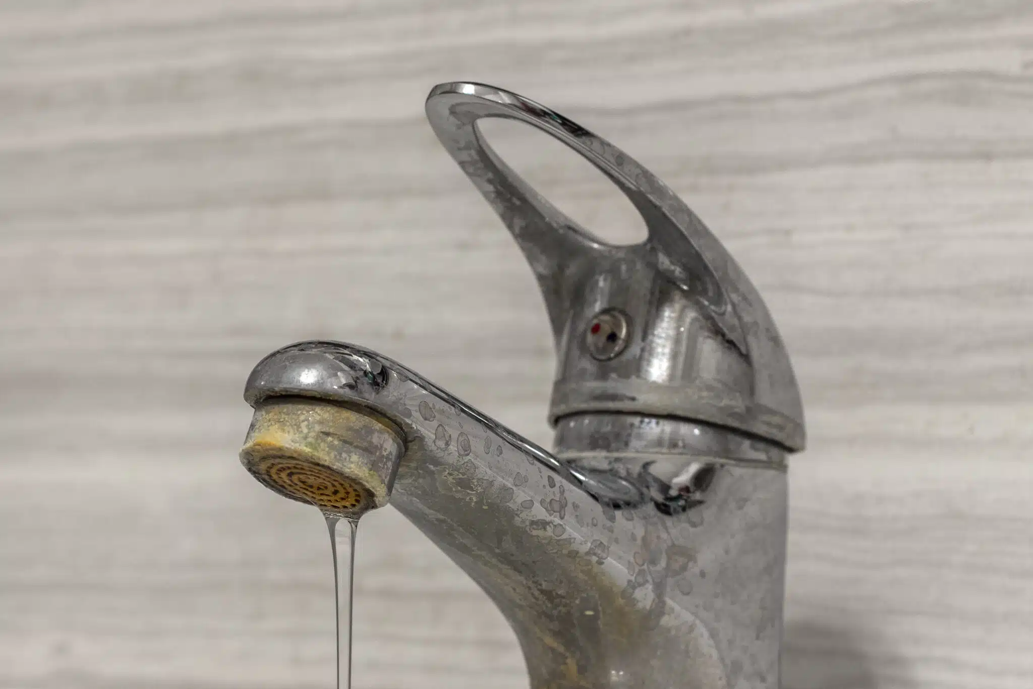 A thin stream of hard water flows from an old tap aerator.