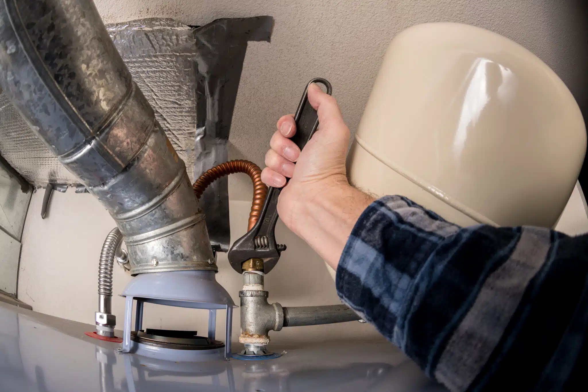 Adjustable wrench tightening a pipe on a water heater by a plumber, Water Heater Maintenance.